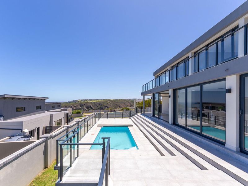 Modern outdoor pool area featuring a sleek swimming pool, expansive tiled terrace, and glass balustrades with panoramic views of the surrounding landscape.