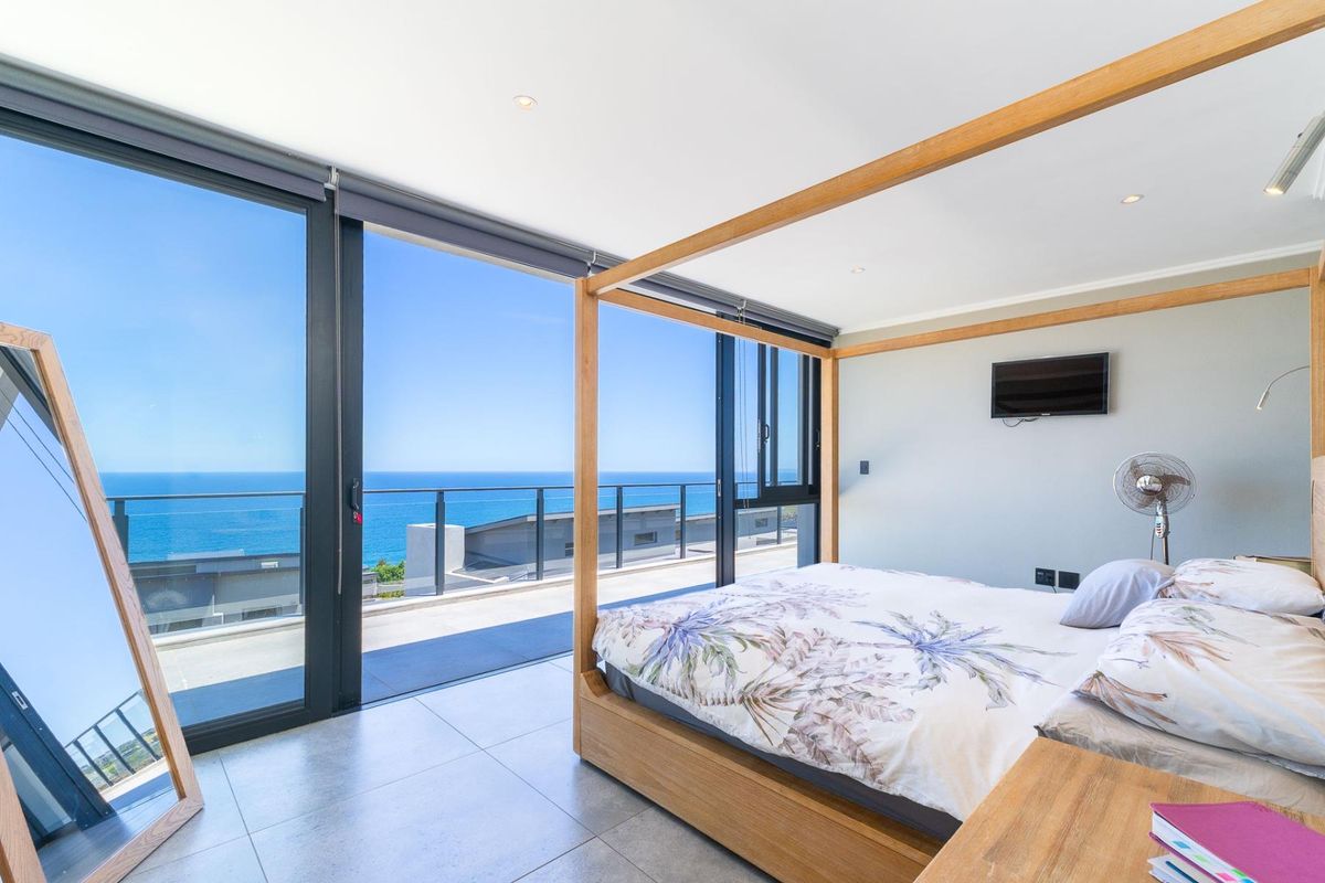 Modern bedroom featuring large sliding glass doors that open onto a balcony with expansive ocean views, tiled flooring, and recessed lighting.