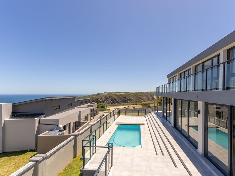 Modern outdoor pool area featuring a tiled patio, glass balustrades, and expansive sliding doors with panoramic coastal views.