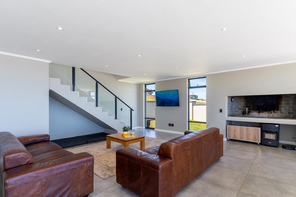 Spacious modern living room featuring tiled floors, recessed lighting, a sleek staircase with glass balustrade, and a built-in fireplace.