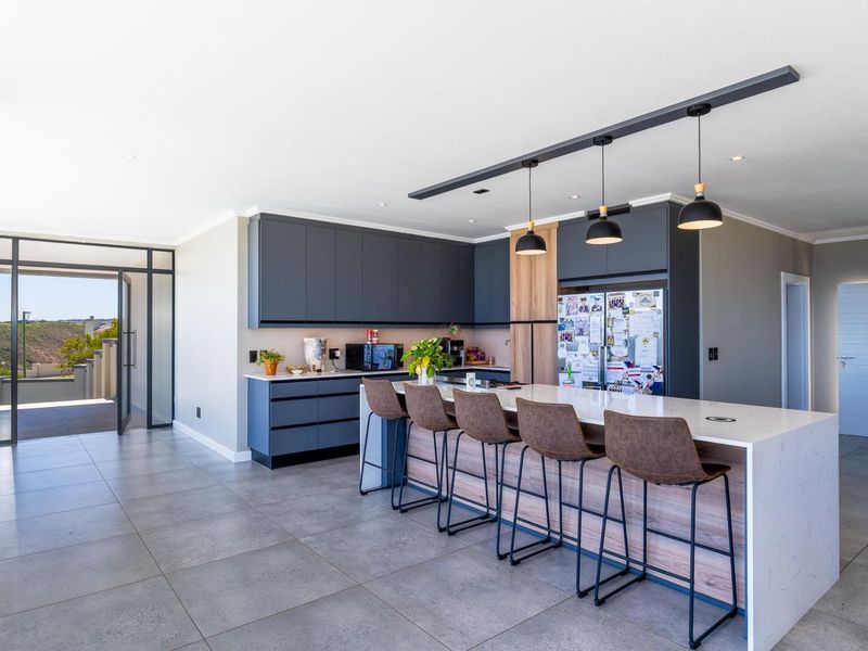 Modern open-plan kitchen featuring a large island with quartz countertops, sleek dark cabinetry, wood-grain accents, and contemporary pendant lighting.