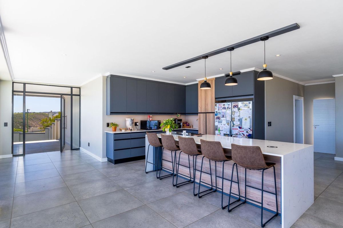 Modern open-plan kitchen featuring a large island with quartz countertops, sleek dark cabinetry, wood-grain accents, and contemporary pendant lighting.