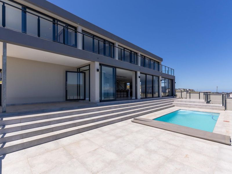 Modern rear exterior featuring a tiled patio, swimming pool, and expansive glass sliding doors leading into the main living area.