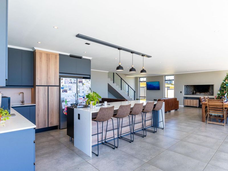 Spacious open-plan living area featuring a modern kitchen with a large island, stone countertops, sleek cabinetry, and a staircase with a glass balustrade.
