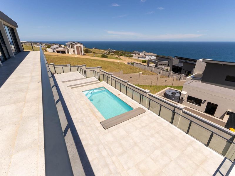 Elevated view of a modern tiled patio area featuring a swimming pool with glass balustrades and expansive coastal views.