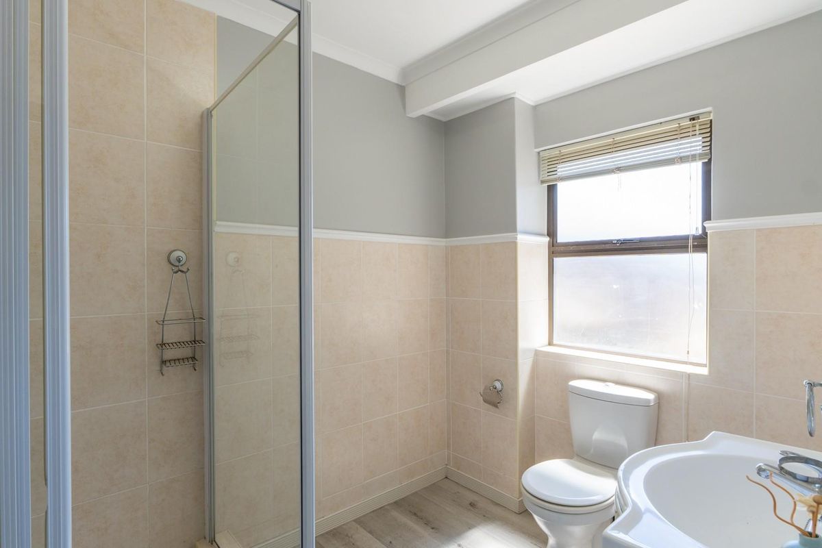 A functional bathroom featuring a glass-enclosed shower, pedestal sink, and toilet, finished with neutral wall tiles and light-toned flooring.