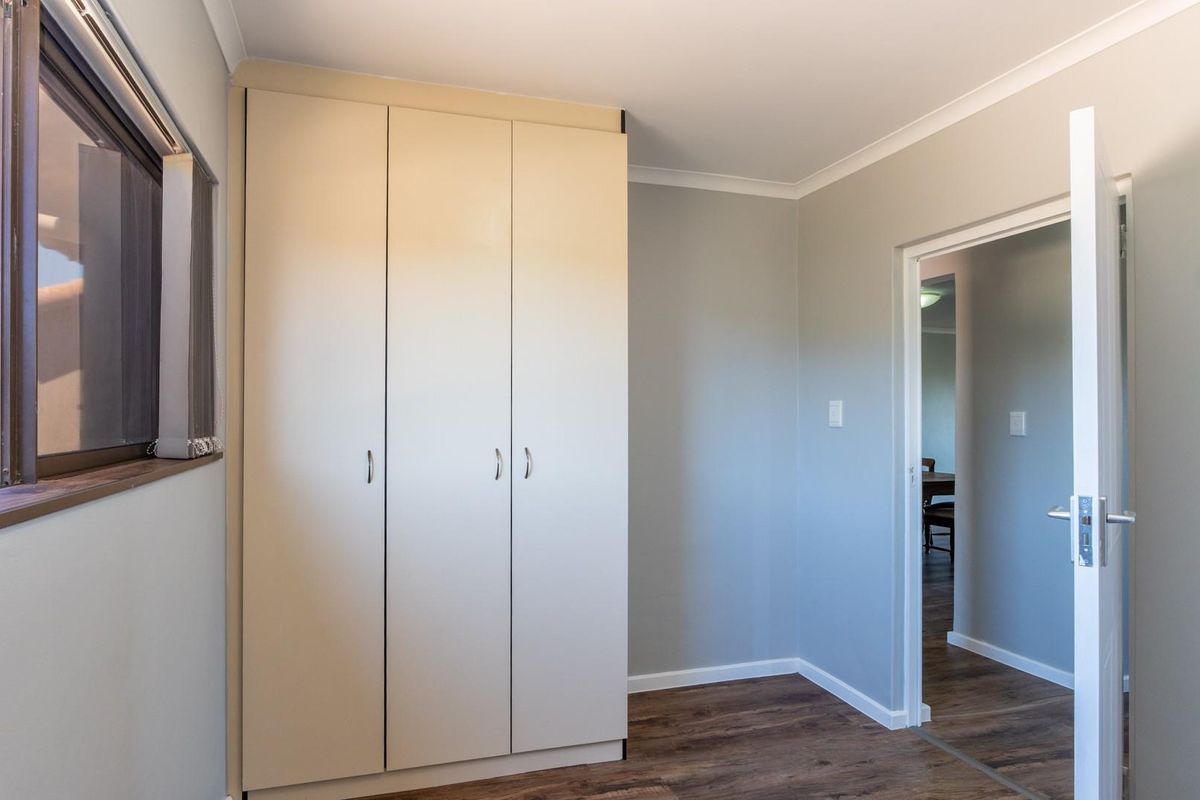 A bedroom featuring built-in cupboards, laminate flooring, and a window with a view of the exterior roofline.