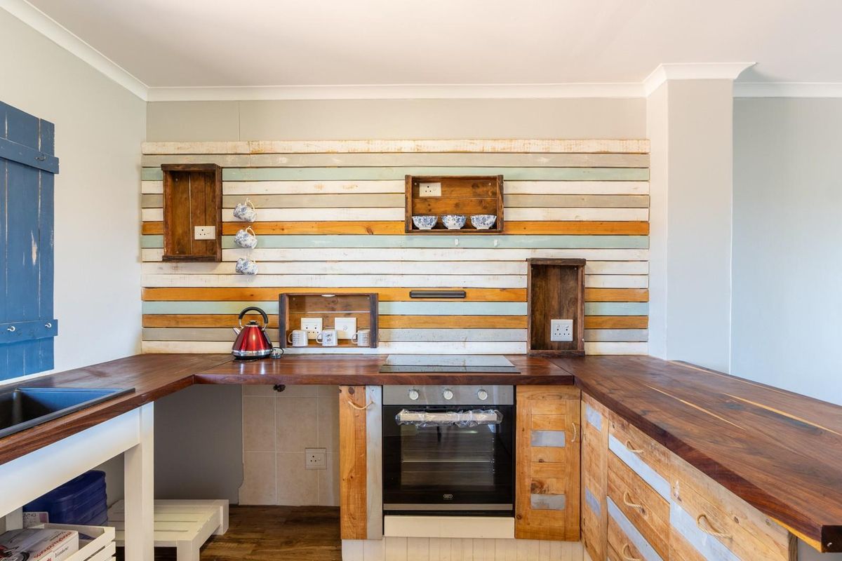 A rustic-style kitchen featuring dark wood countertops, a built-in oven, and a decorative multi-colored timber plank backsplash with integrated shelving.