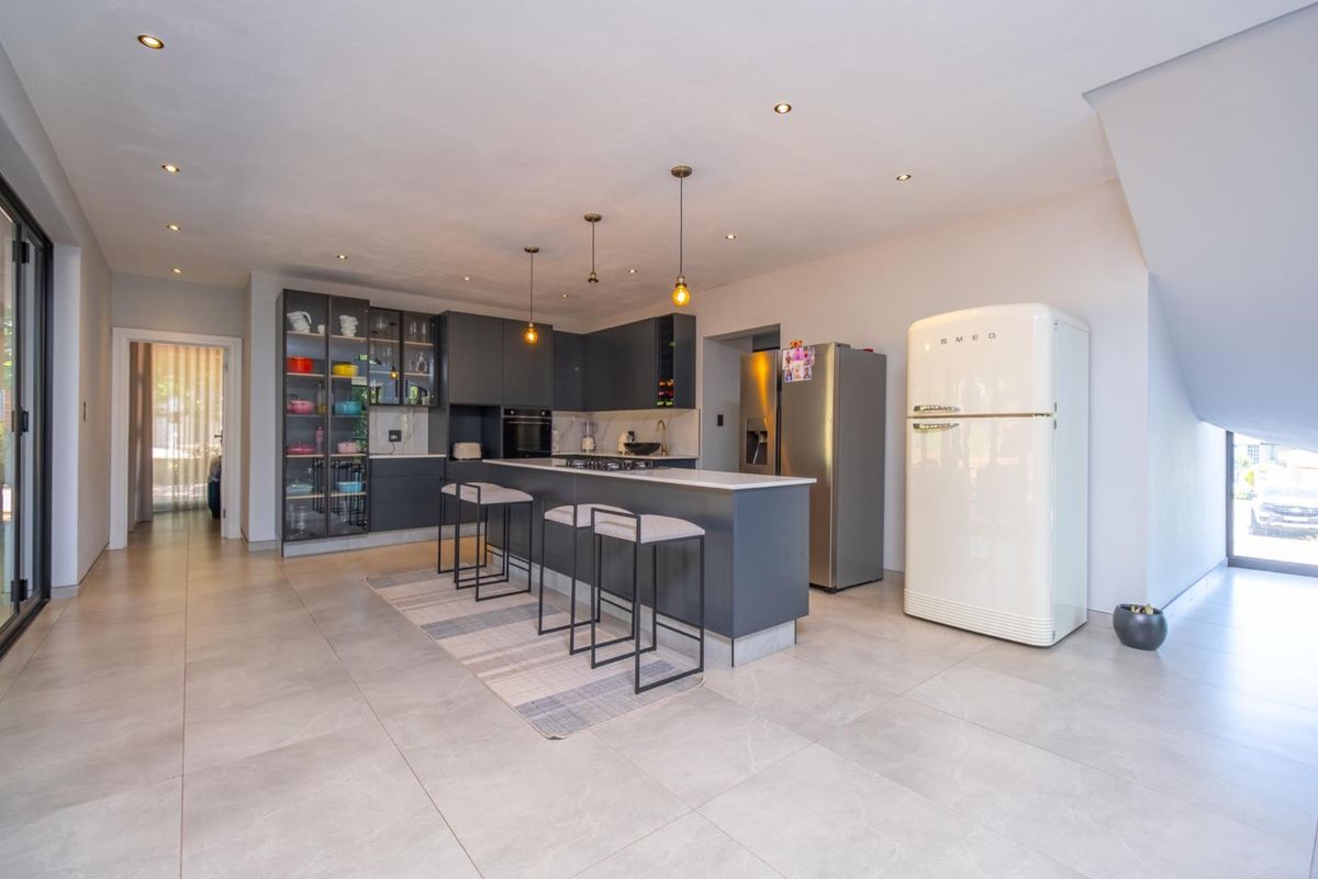 Modern open-plan kitchen featuring dark cabinetry, a central island with breakfast bar, stone countertops, and high-quality integrated appliances.