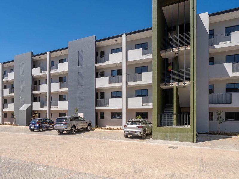 Modern multi-story apartment complex featuring a paved parking area, private balconies with metal railings, and a prominent external stairwell.