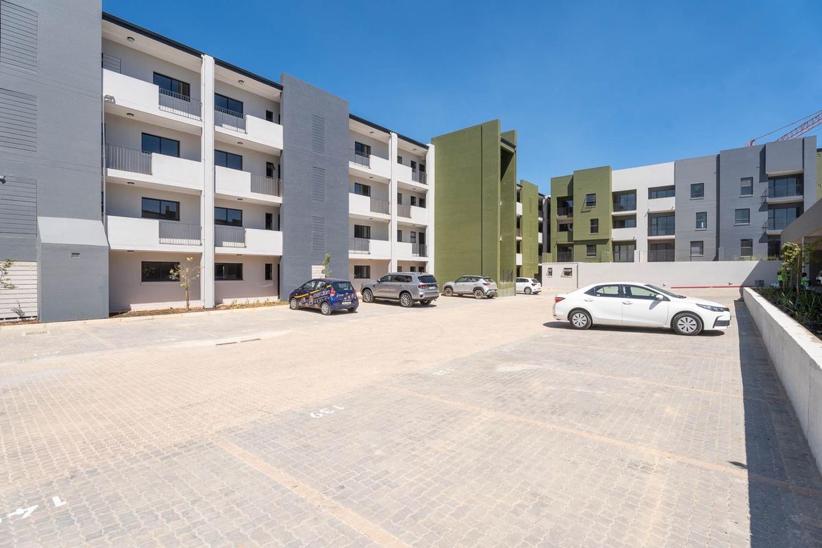 A view of the paved parking area and the rear facade of a modern multi-story apartment complex.