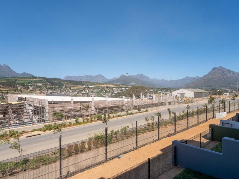 Elevated view overlooking a suburban street, security fencing, and ongoing construction site with scenic mountain range in the background.