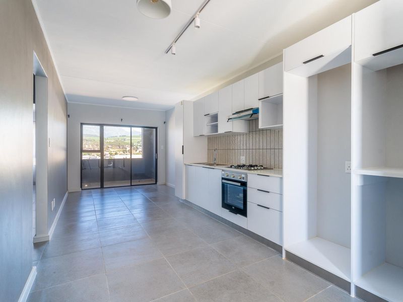 Modern open-plan kitchen and living area featuring sleek white cabinetry, built-in appliances, tiled flooring, and access to a balcony with scenic views.