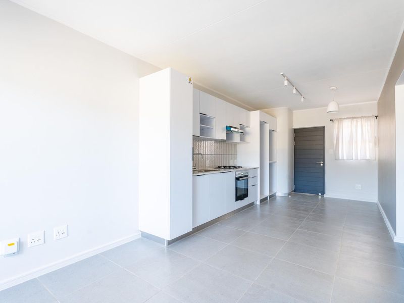 Modern open-plan kitchen and living area featuring sleek white cabinetry, integrated appliances, tiled flooring, and neutral finishes throughout.