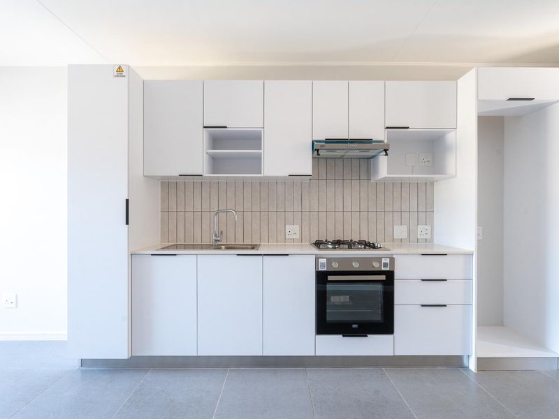 Modern, minimalist kitchen featuring white cabinetry, stone countertops, a gas hob, built-in oven, and a sleek tiled backsplash.