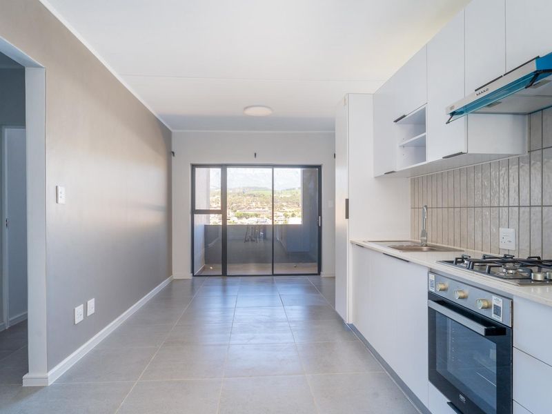 Modern open-plan kitchen and living area featuring tiled floors, built-in cabinetry, gas hob, and sliding glass doors leading to a balcony.