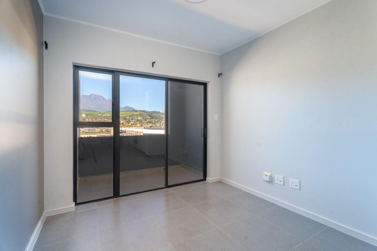 A bright, empty bedroom featuring neutral tiled flooring, modern sliding glass doors, and scenic mountain views.