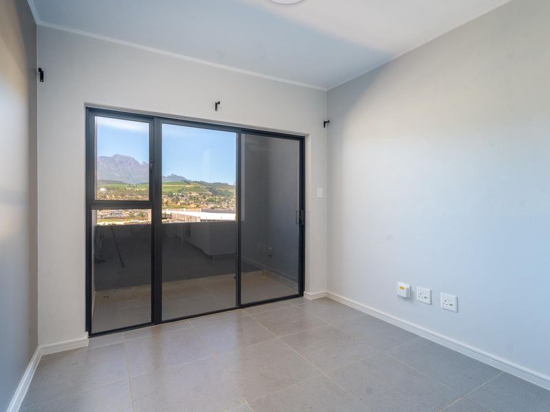 A bright, empty bedroom featuring neutral tiled flooring, modern sliding glass doors, and scenic mountain views.