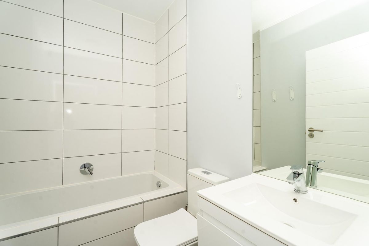 A clean, modern bathroom featuring white wall tiles, a built-in bathtub, a vanity with an integrated sink, and a large wall mirror.