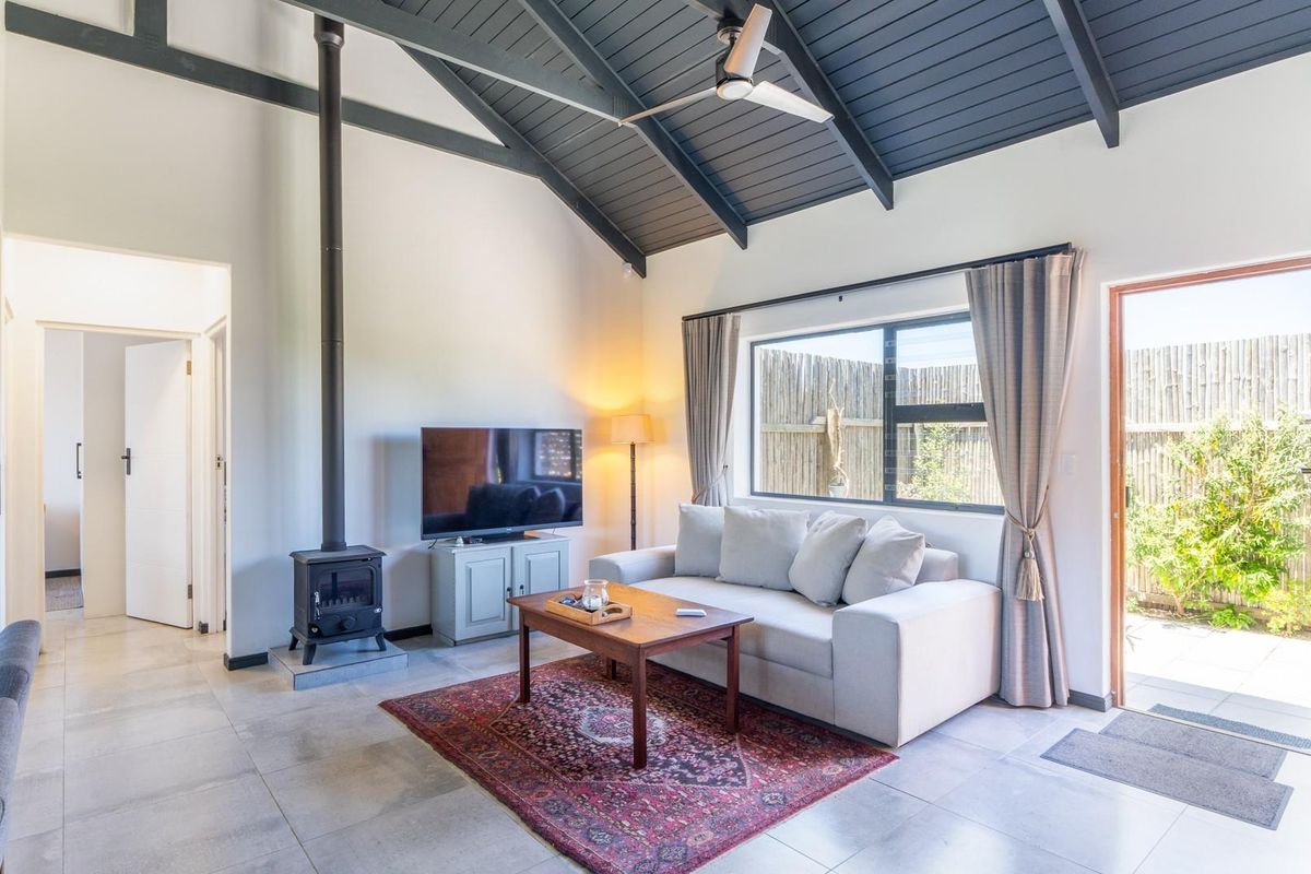 Bright living room featuring a vaulted timber-clad ceiling, a freestanding wood-burning fireplace, tiled flooring, and direct access to the outdoor patio area.