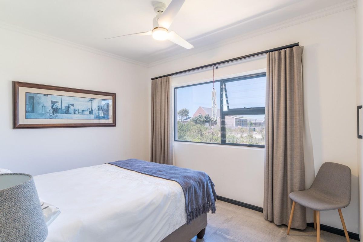 A bright and well-maintained bedroom featuring a ceiling fan, large window with neutral curtains, and built-in cabinetry.