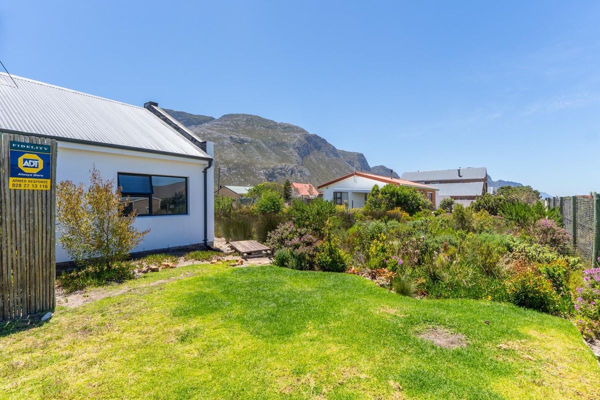 A view of the rear garden and side elevation of the house, featuring a lawn, established landscaping, and mountain views in the background.