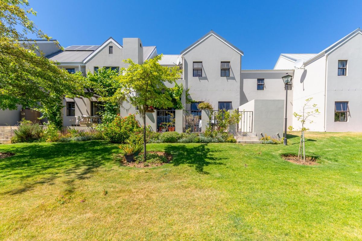 Rear view of a townhouse featuring a well-maintained garden, established landscaping, and solar panels installed on the roof.