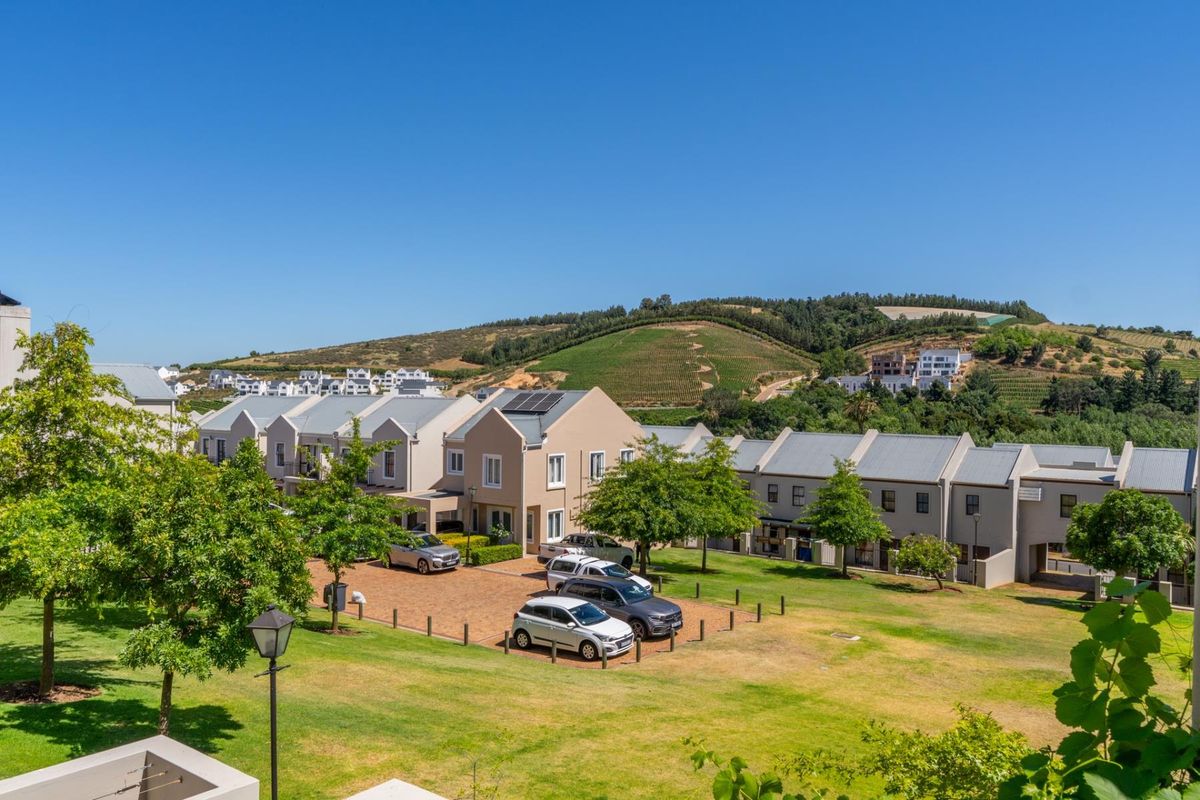 An elevated aerial view of a townhouse complex featuring paved driveways, communal green spaces, and scenic hillside views.
