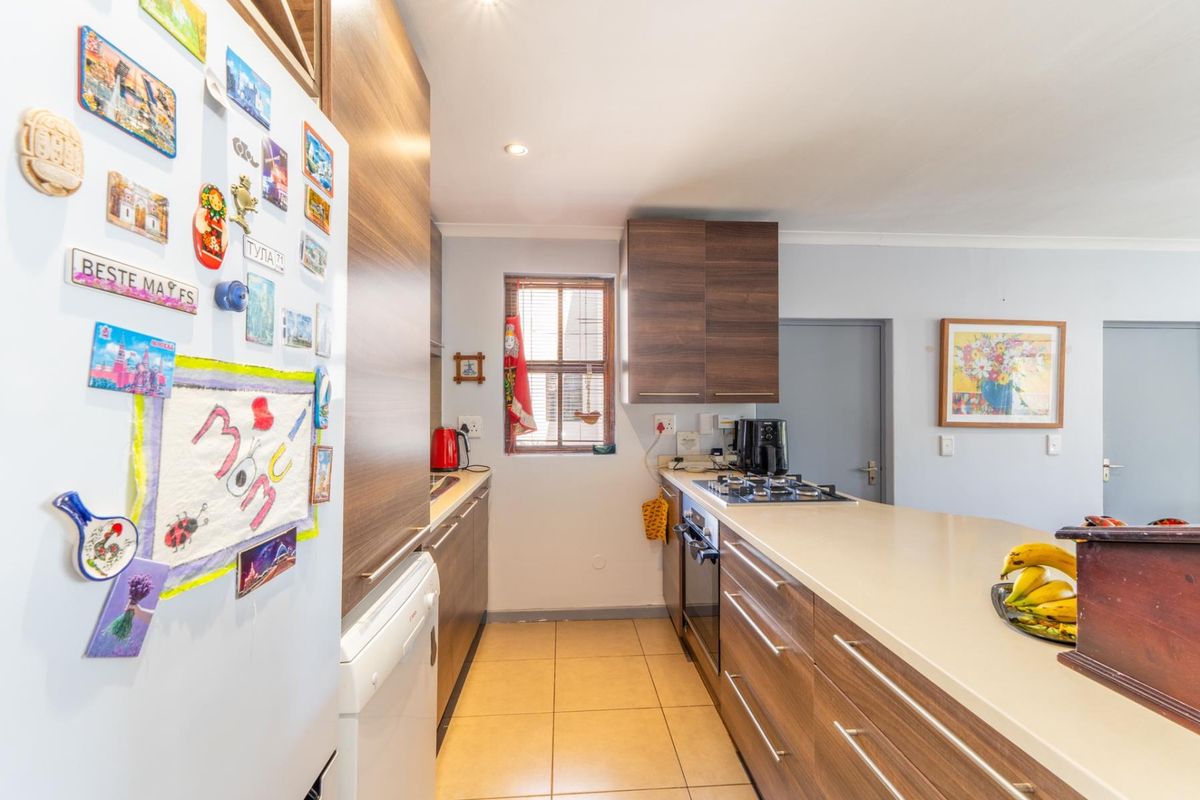 A functional kitchen featuring modern wood-finish cabinetry, stone countertops, a gas hob, and built-in oven with tiled flooring.