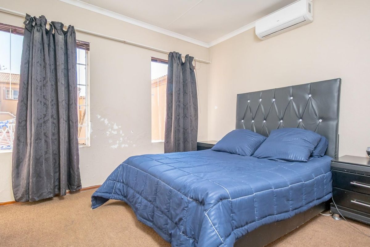 A bedroom featuring a wall-mounted air conditioning unit, carpeted flooring, and dual windows with curtain tracks.