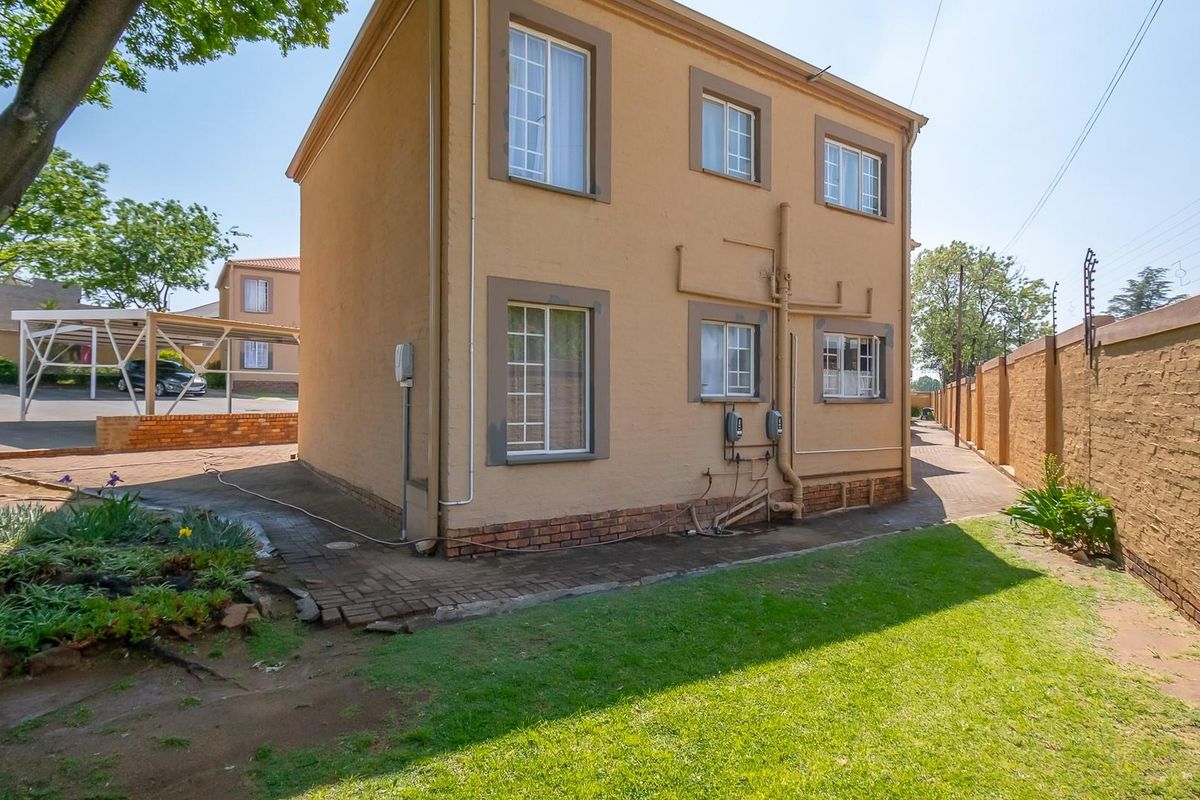 Side view of a double-story townhouse featuring a plastered facade, paved walkway, and a small private garden area with perimeter walling.