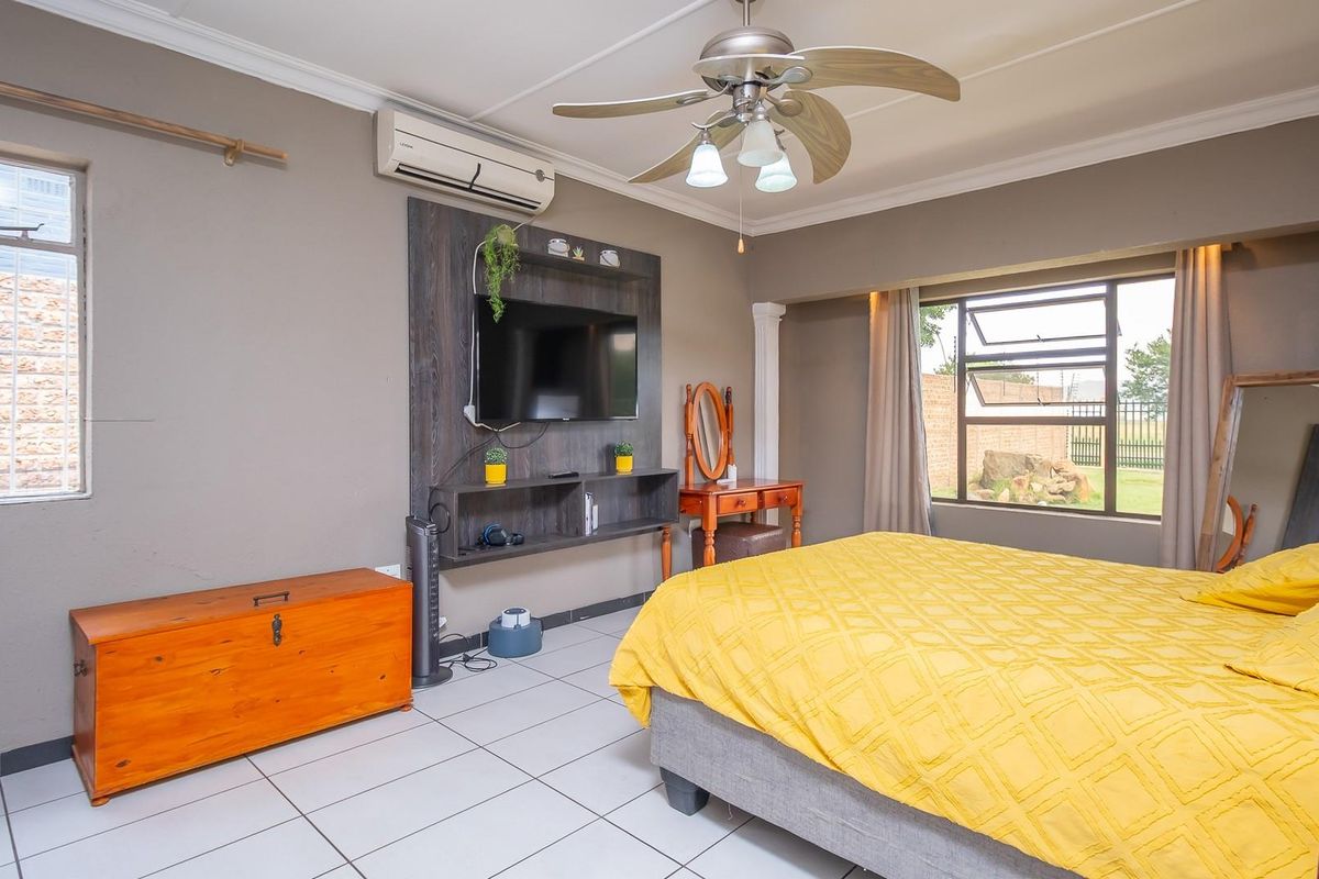A spacious bedroom featuring tiled flooring, a ceiling fan, wall-mounted air conditioning unit, and a built-in media console.