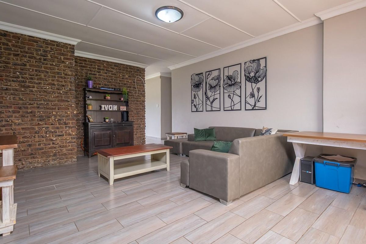 Spacious living room featuring a prominent exposed brick feature wall, modern wood-look floor tiles, and a clean, neutral color palette.