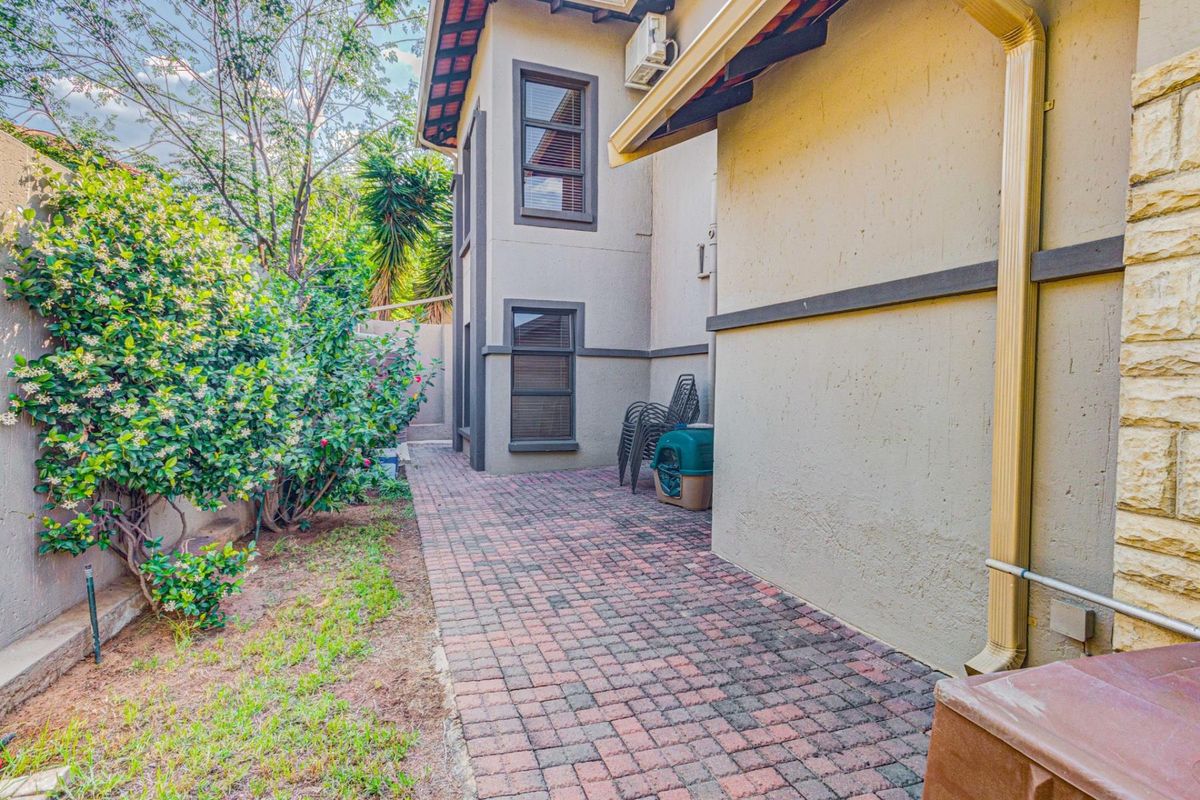 A side exterior view of the property featuring paved walkways, established garden landscaping, and a multi-story building facade with integrated air conditioning unit.