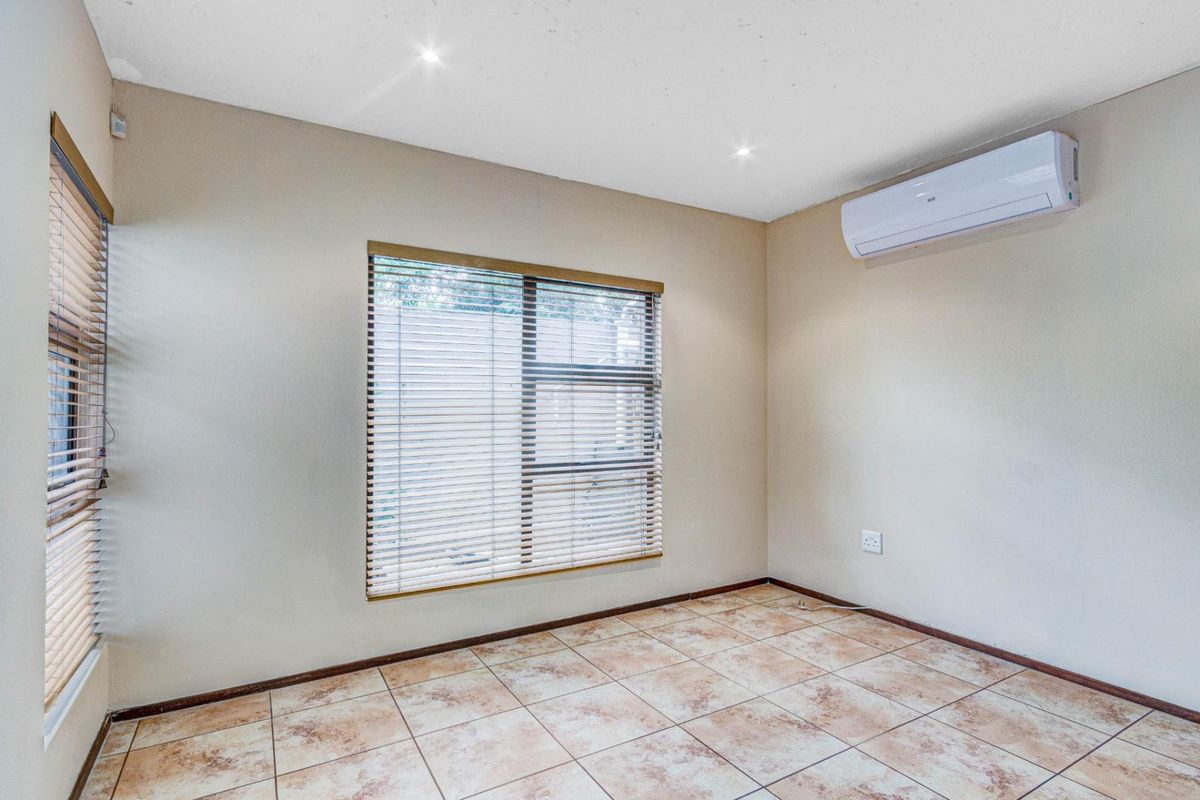 A bright, empty bedroom featuring neutral wall tones, tiled flooring, recessed ceiling lighting, and a wall-mounted air conditioning unit.