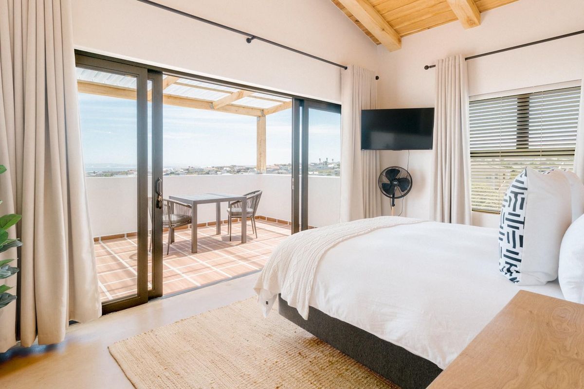 Bright bedroom featuring vaulted timber ceilings, large sliding glass doors, and direct access to a private balcony with scenic coastal views.