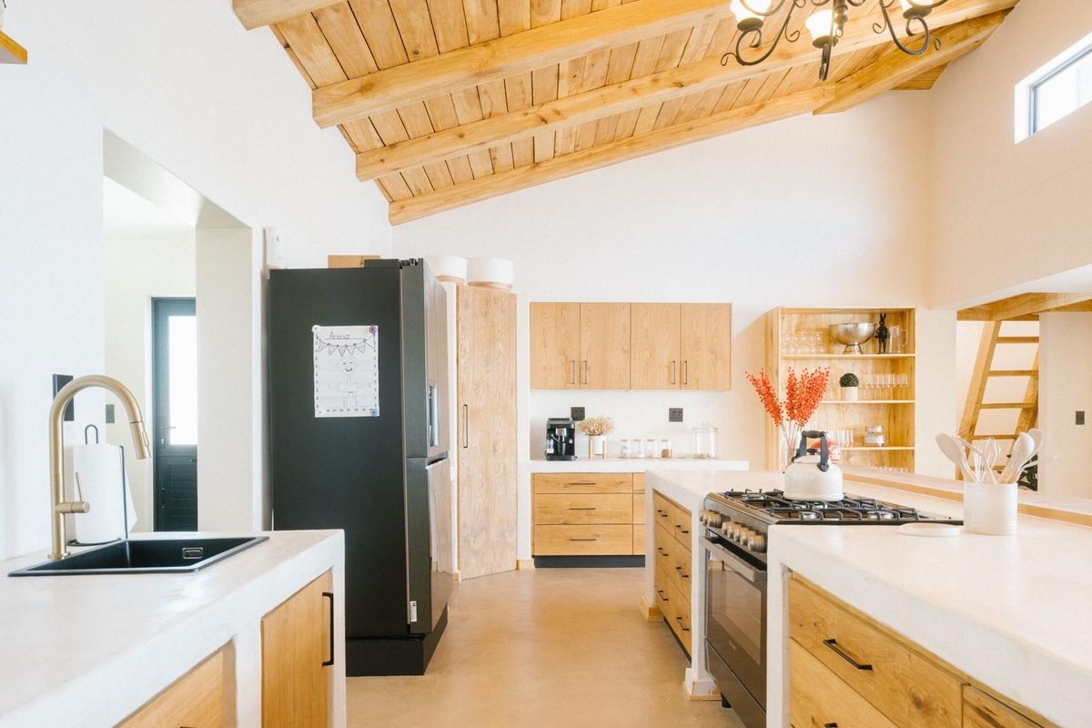 Modern kitchen featuring light wood cabinetry, concrete-style countertops, a gas cooktop, and exposed timber ceiling beams in a bright, open-plan layout.