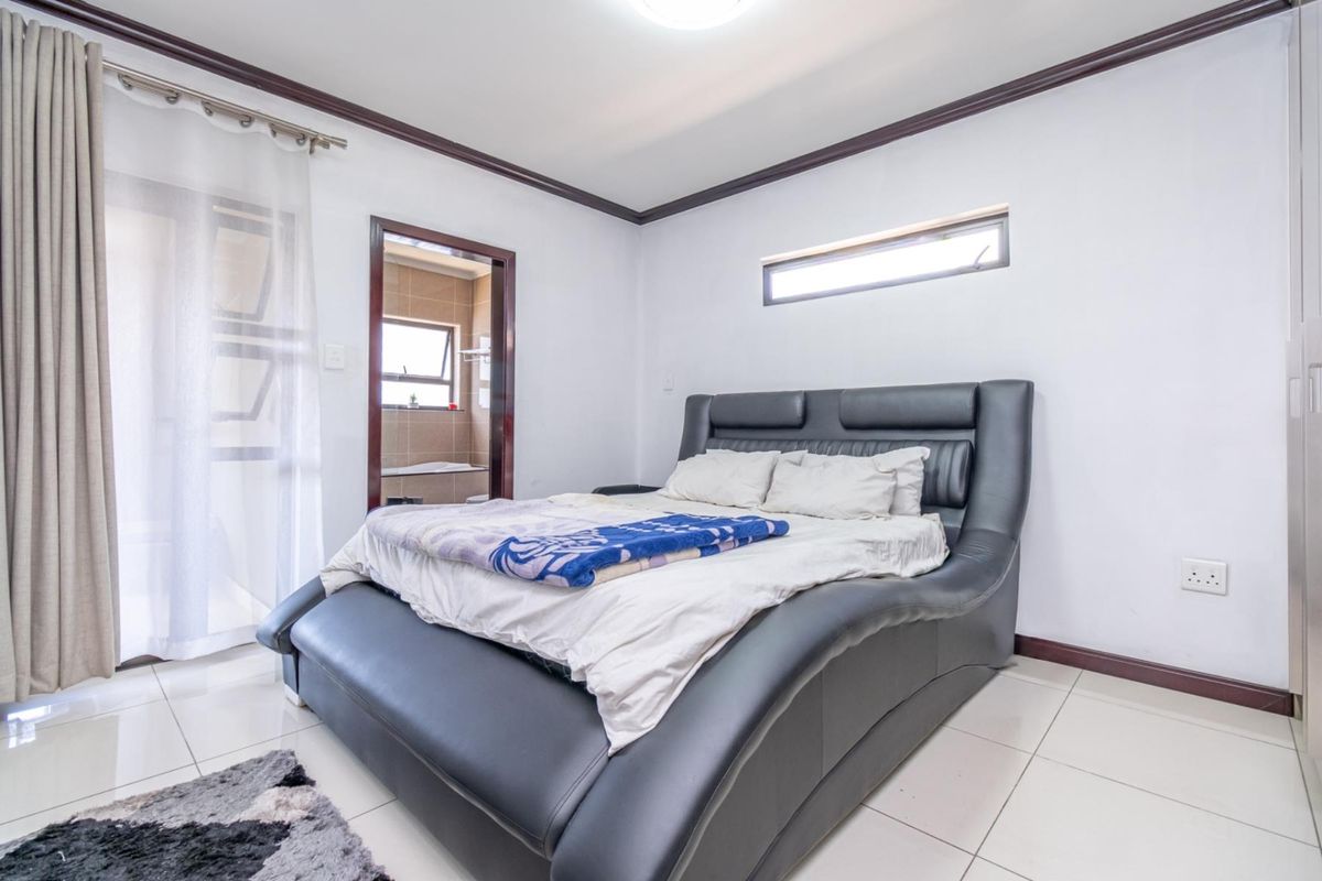 A well-lit bedroom featuring tiled flooring, dark wood trim, and an en-suite bathroom access point.