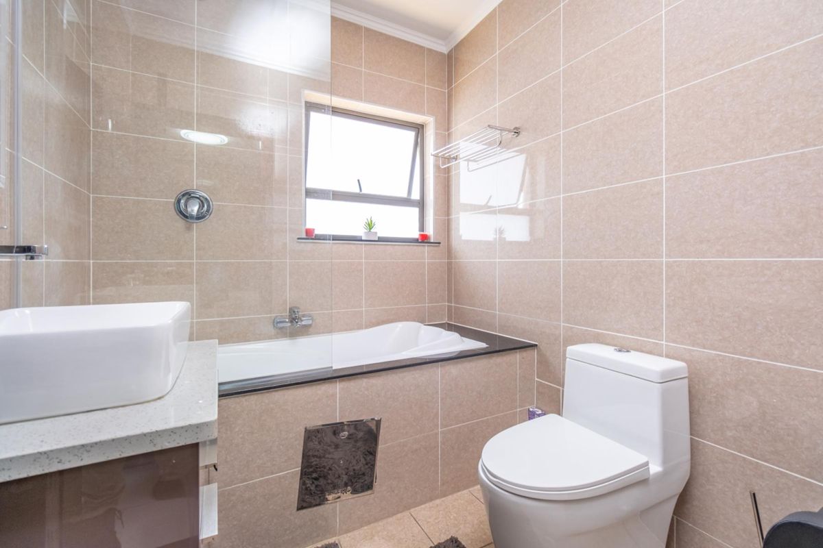 A modern bathroom featuring a built-in bathtub with a glass screen, a vanity basin, and a toilet, finished with neutral wall and floor tiling.