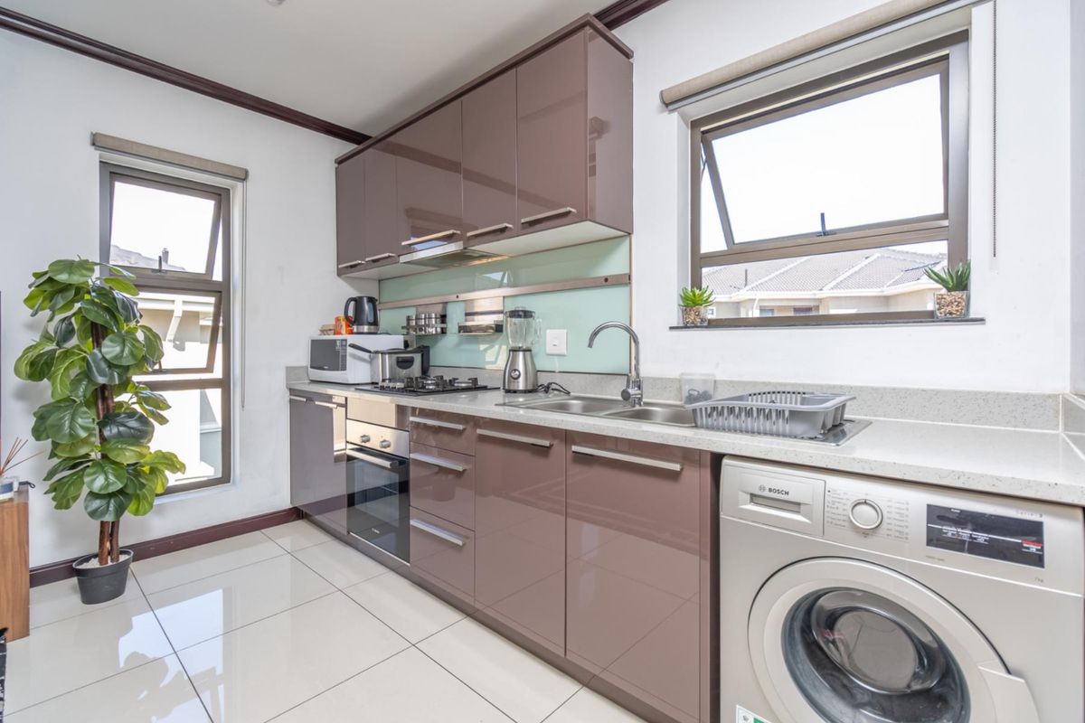 Modern kitchen featuring high-gloss cabinetry, stone countertops, integrated stainless steel oven, gas hob, extractor fan, and space for a front-loading washing machine.
