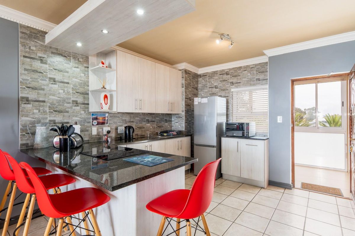 Modern kitchen featuring stone-cladding backsplash, granite countertops, built-in cabinetry, and a breakfast bar, with direct access to an outdoor patio area.