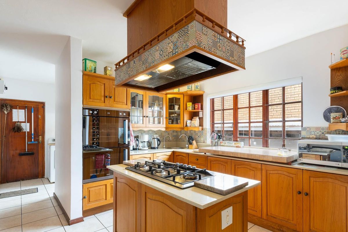 A traditional kitchen featuring wooden cabinetry, a central island with a gas hob, and a decorative overhead extractor fan.