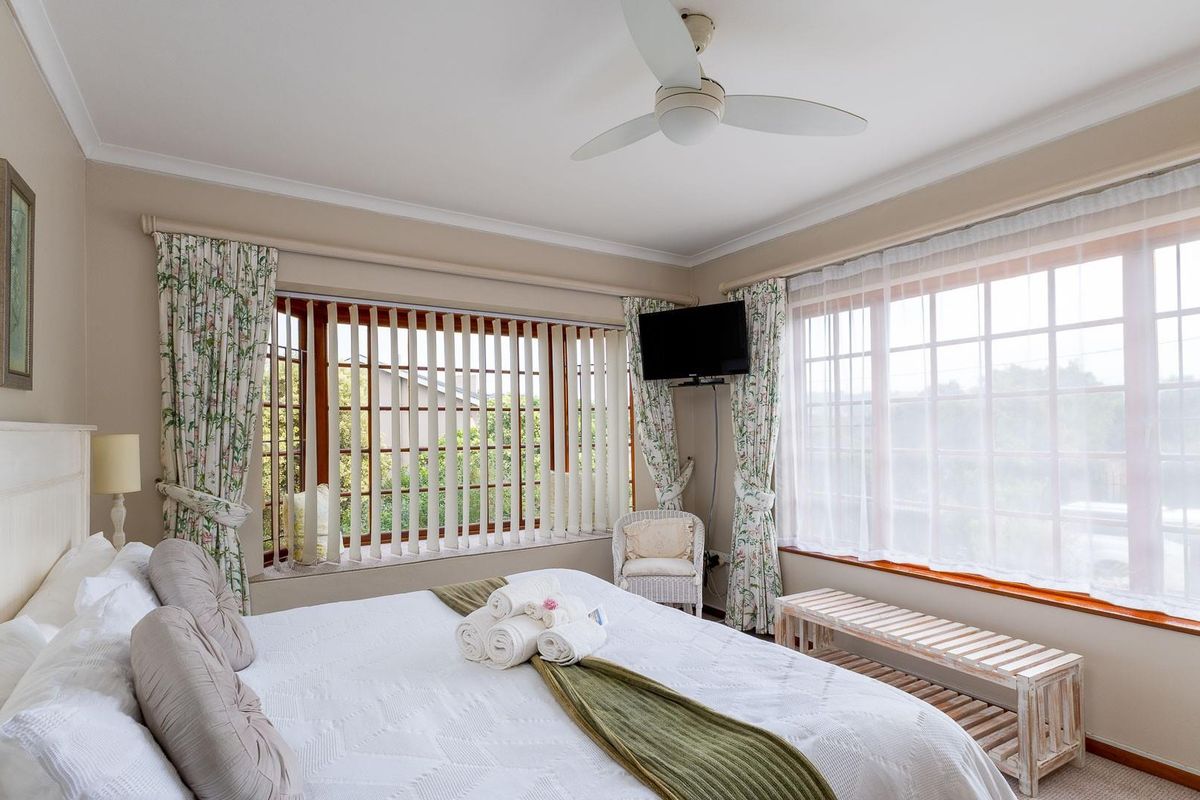 A well-lit bedroom featuring large windows with vertical blinds, a ceiling fan, and neutral wall finishes.