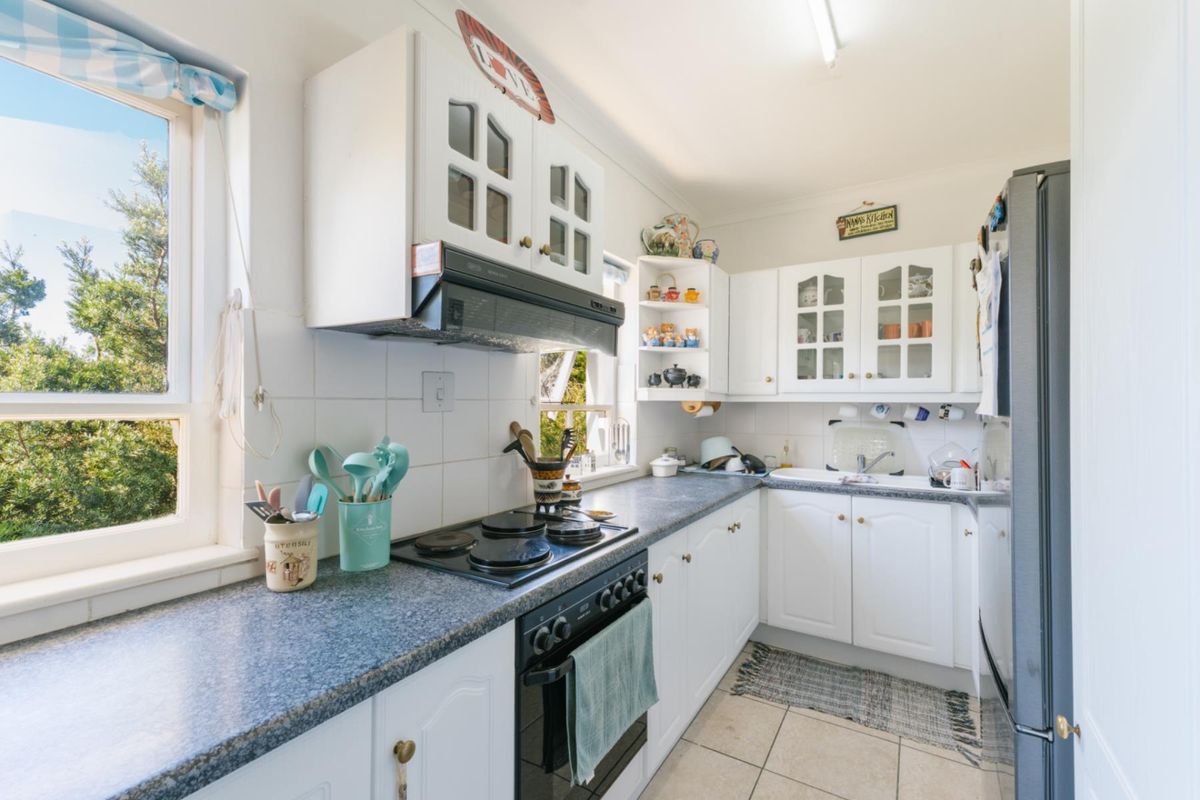 A functional kitchen featuring white cabinetry, dark laminate countertops, a built-in electric hob, and an integrated oven with an extractor fan.