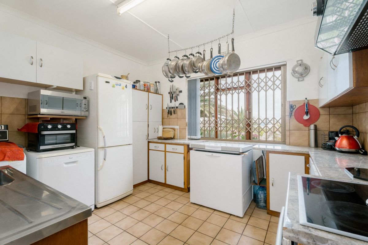 Functional kitchen featuring laminate countertops, built-in cabinetry, tiled flooring, and a window with security gate, offering a practical layout for daily meal preparation.