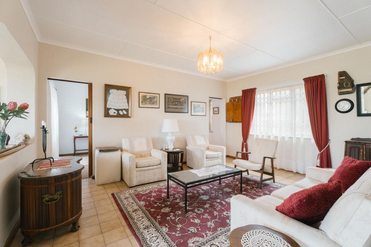 A traditional living room featuring tiled flooring, a central chandelier, and large windows with curtains, providing a comfortable and well-lit living space.
