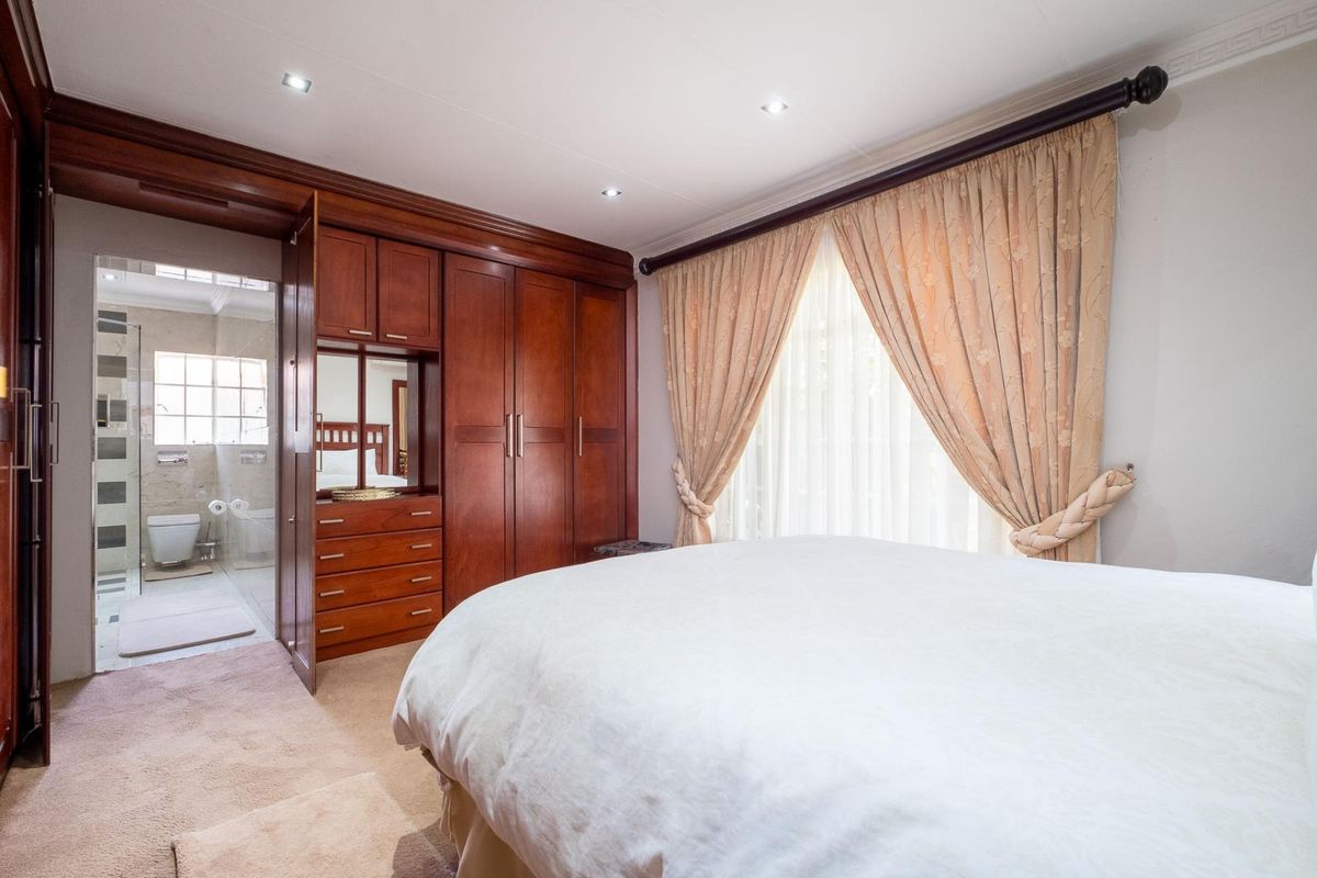 Spacious bedroom featuring extensive built-in wooden cabinetry and an en-suite bathroom with modern tiling and fixtures.