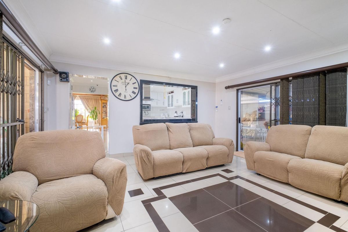 Spacious living room featuring tiled flooring with decorative inlay, recessed downlighting, and a serving hatch opening into the kitchen area.