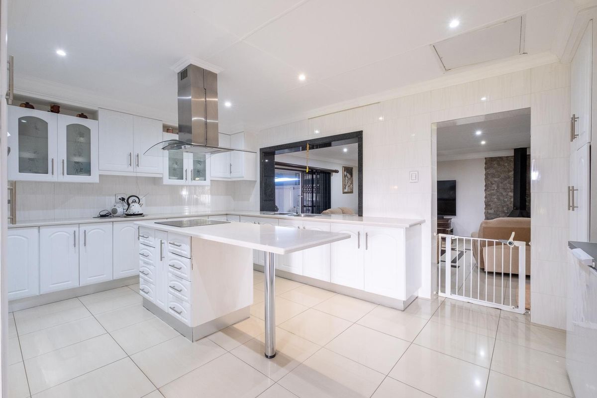 Modern kitchen featuring white cabinetry, a central island with breakfast bar, stainless steel extractor fan, and tiled flooring.