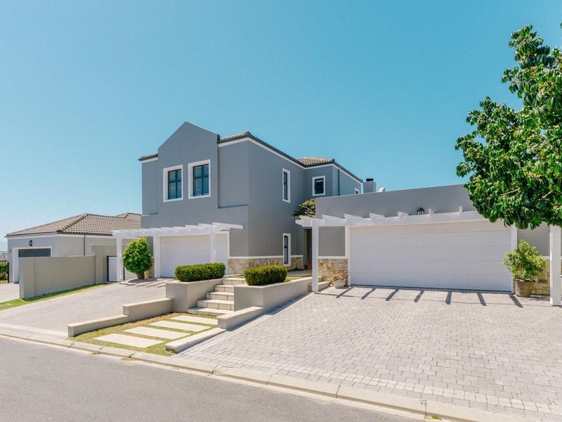 Modern double-story residential home featuring a paved driveway, double garage, and decorative pergola structures with stone cladding accents.